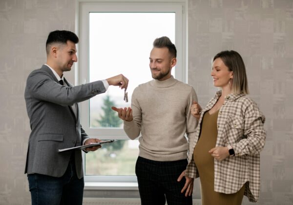 A pregnant woman and her partner receive house keys from a real estate agent indoors.
